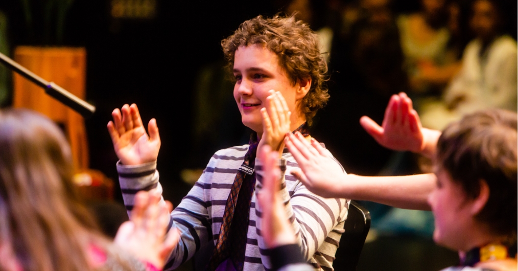 A photo of a boy in a striped long sleeve T-shirt clapping in a circle with others