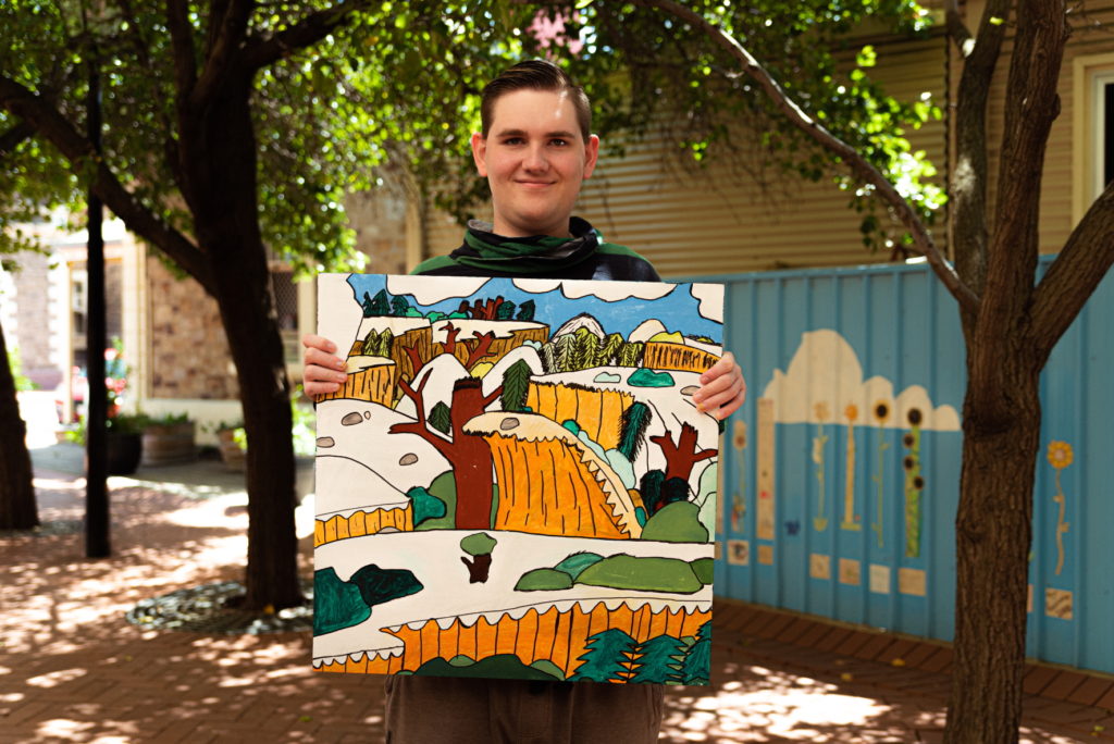 A photo of a man standing outside, holding an artwork with an animation aesthetic
