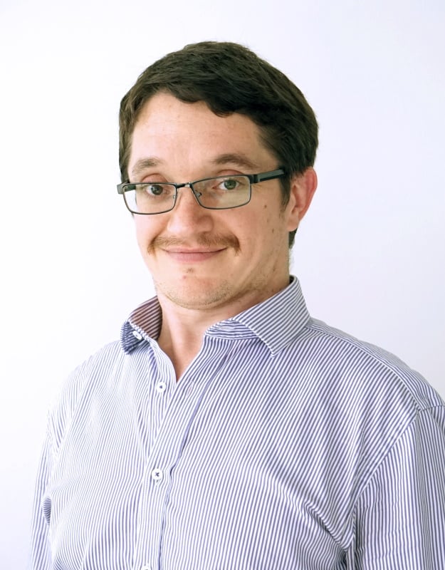 A head and shoulders portrait photo of a man with a moustache wearing glasses and a striped business shirt