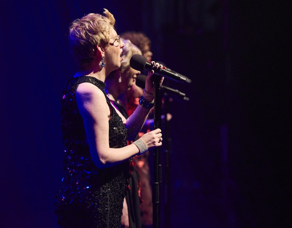 A group of women on stage singing into microphones