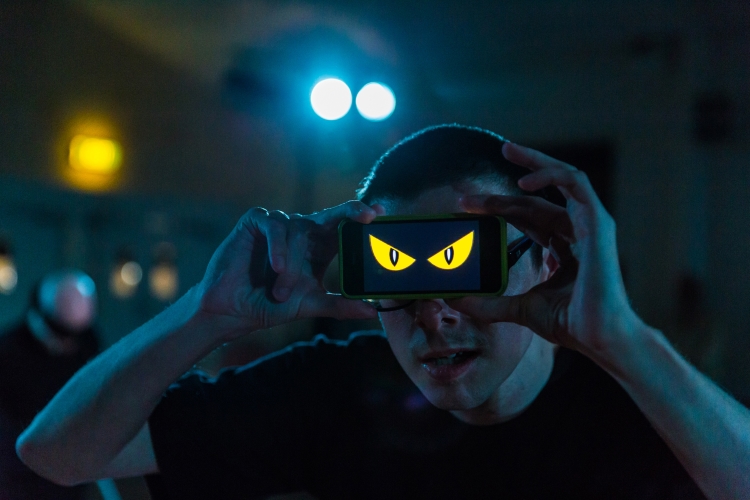 A man holds a phone in front of his face showing an image of two yellow eyes